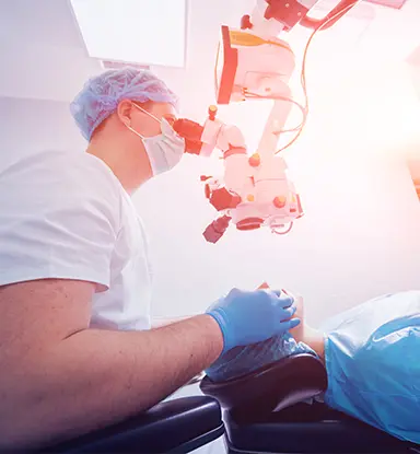 Lasik: An optometric physican wearing surgical cap, mask, and gloves uses a ceiling mounted device to examine a patient lying in front of him.
