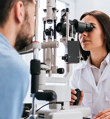 Primary Eye Care: A female female optometric physican is using a device to examine a bearded man's eyes.