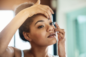 A woman put in contacts, contemplating the benefits of LASIK vs contact lenses for her vision correction needs.