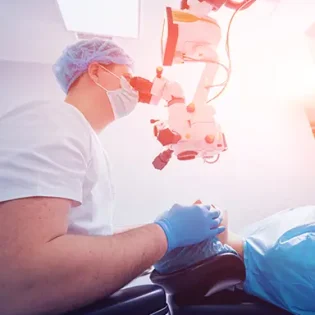 Lasik: An optometric physican wearing surgical cap, mask, and gloves uses a ceiling mounted device to examine a patient lying in front of him.